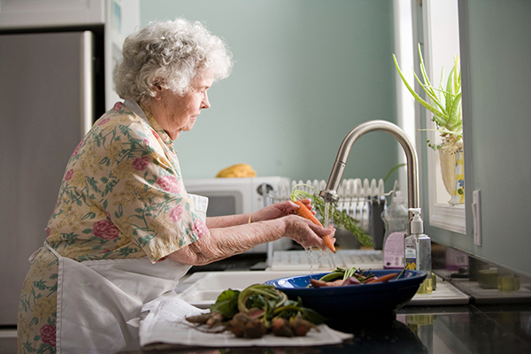 Older woman washing vegetables at sink